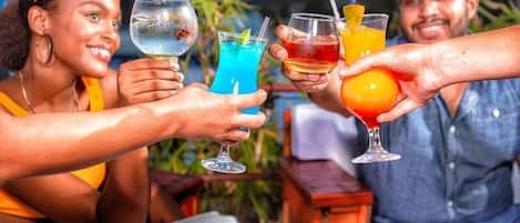 A group of people toasting with colorful drinks at an outdoor setting with a cityscape in the background.