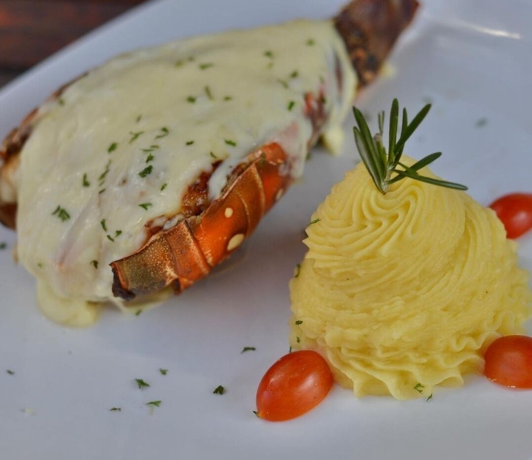 A lobster tail with melted butter and a side of mashed potatoes garnished with herbs and cherry tomatoes.