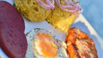 A plate with a fried egg, a slice of sausage, a piece of fried plantain, and a small mound of food topped with red onion slices.