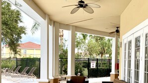 A covered outdoor seating area with wicker furniture, a ceiling fan, and a view of a pool and greenery. - Gated, NO stairs, NO carpet 1 min walk to lakefront POOL, PICKLEBALL/TENNIS (Sarasota)