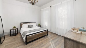 A bedroom with a wooden bed, a small bedside table with a plant, a chandelier, and a wooden dresser with decorative items. -  New/Midtown Sac/Free Parking/Coffee/Long stays welcomed (Sacramento)