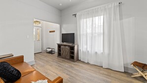 A modern living room with a wooden entertainment unit, a flat-screen TV, a ceiling fan, and a large window with white curtains. -  New/Midtown Sac/Free Parking/Coffee/Long stays welcomed (Sacramento)