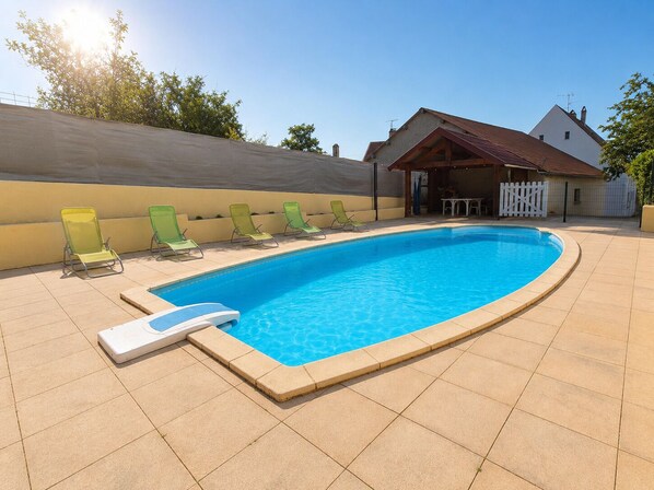 Une piscine avec un plongeoir, entourée de chaises longues, et une terrasse couverte.