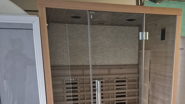 A glass-enclosed sauna with a wooden interior, metal handles, and ventilation slats.