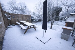 Un espace extérieur enneigé avec des tables de pique-nique et un parasol noir.