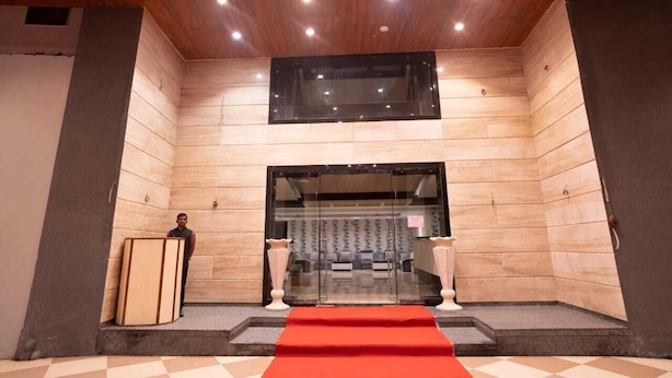 A hotel lobby with a red carpet, a reception desk, and a large TV screen on the wall.