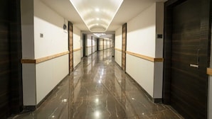 A long, well-lit hallway with marble flooring, wooden trim, and dark doors.