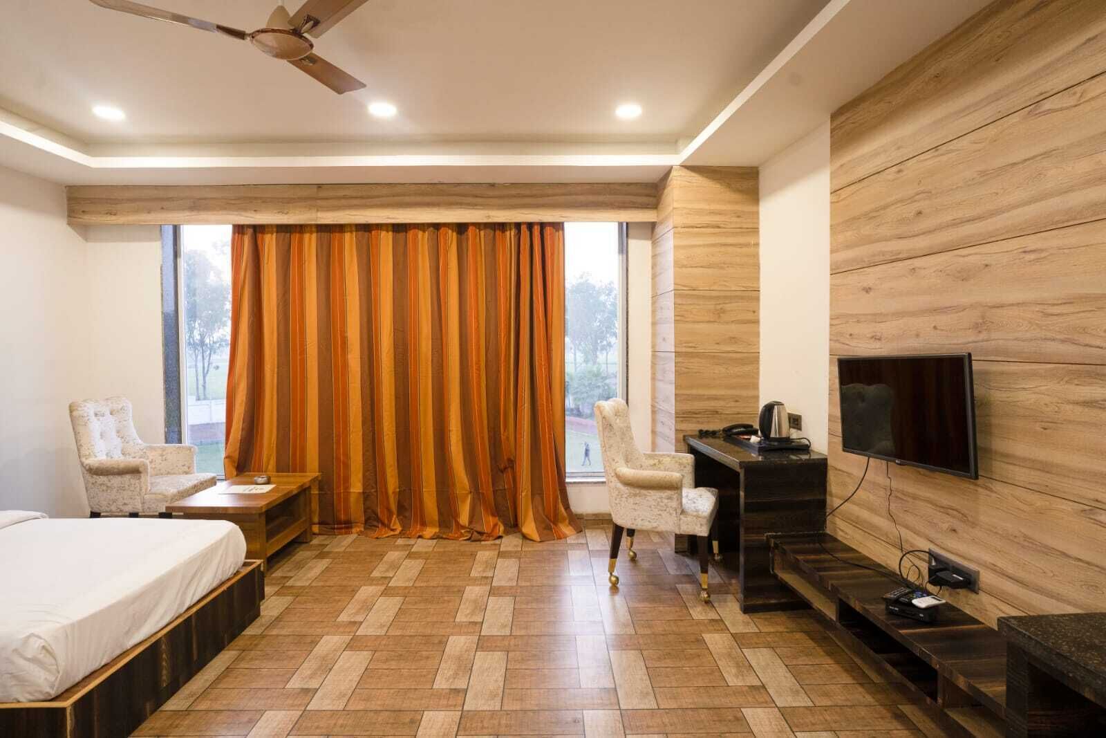 A modern hotel room with a wooden floor, a bed, a desk with a TV, a chair, and a window with curtains.