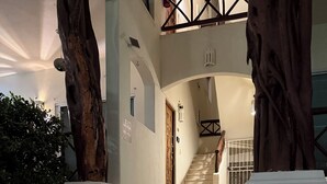 A staircase leading to a door with a 'NO ESTACIONARSE' sign, flanked by large trees and a tiled floor.