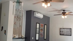 A living room with a beige sofa, a ceiling fan, and wall-mounted air conditioning.