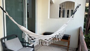 A balcony with a hammock, a chair, a small table, and a potted plant.