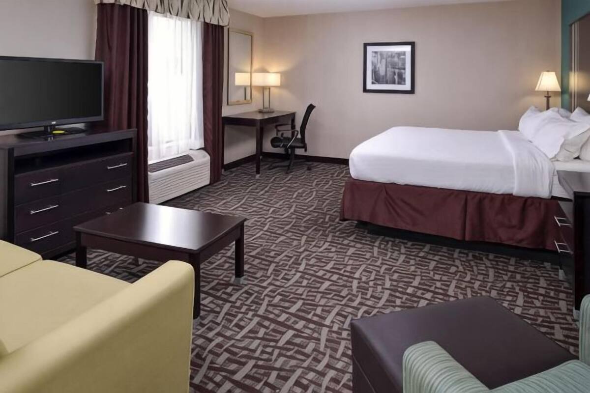 A hotel room with a bed, a desk, a television, a chair, and a sofa.
