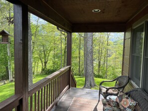 A wooden deck with a railing, wicker furniture, and a view of a forest.