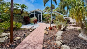 A tropical resort with a paved pathway leading to a building with large windows and a covered entrance. - Private Oasis at the Beach with HEATED Pool, Dock and Boat…..Dolphin paradise! (Cocoa Beach)