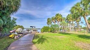 A wooden dock leading to a boat, surrounded by palm trees and a grassy area. - Private Oasis at the Beach with HEATED Pool, Dock and Boat…..Dolphin paradise! (Cocoa Beach)