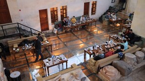 Un'ampia sala da pranzo interna con diversi tavoli e sedie, uno spazio aperto centrale e colonne in pietra.