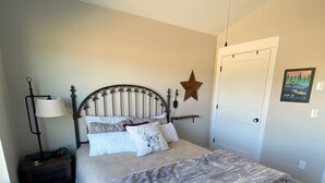 A bedroom with a bed, a ceiling fan, a nightstand, a lamp, a star decoration, and a door. - Quiet Country Setting (Bozeman)