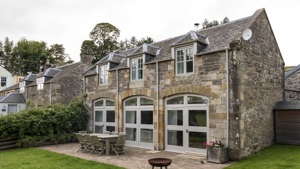 A stone building with a patio area, including a table and chairs, and a wheelbarrow. - The Coach House, Pentland Hills - Sleeping 6 Guests in 3 Bedrooms, Dog Friendly (Nine Mile Burn)
