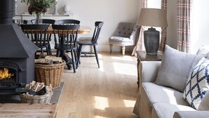 A cozy living room with a fireplace, wooden flooring, a dining area with a table and chairs, and a sofa with cushions. - The Coach House, Pentland Hills - Sleeping 6 Guests in 3 Bedrooms, Dog Friendly (Nine Mile Burn)