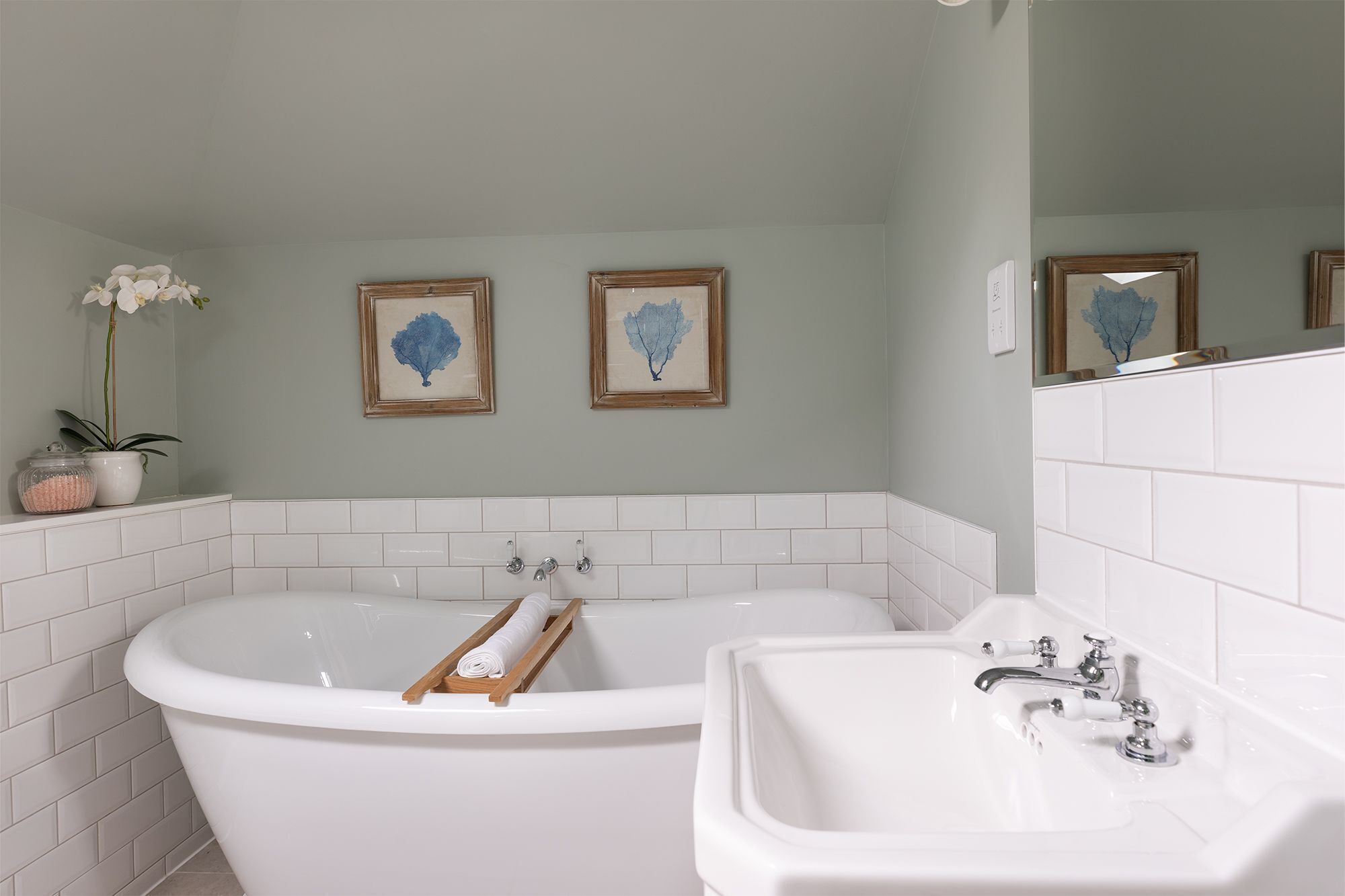 A bathroom with a freestanding bathtub, a sink, and two framed wall art pieces.