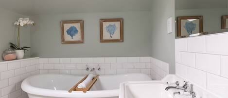 A bathroom with a freestanding bathtub, a sink, and two framed wall art pieces.
