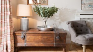 A wooden chest with a metal bowl and a vase of green foliage, a lamp, and a grey upholstered chair. - The Coach House, Pentland Hills - Sleeping 6 Guests in 3 Bedrooms, Dog Friendly (Nine Mile Burn)