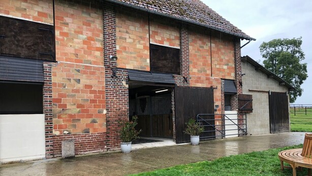 Un bâtiment en briques doté d’une entrée couverte, d’une terrasse en béton et d’un espace verdoyant avec un banc en bois.
