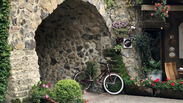 Un edificio de piedra con un amplio arco de entrada, una bicicleta estacionada afuera y macetas con flores.