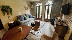 Una sala acogedora con sofá, una mesa de comedor y sillas, chimenea y ventanas amplias.