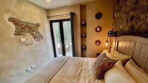 Un dormitorio con una cama grande, una pared de piedra, una ventana con cortinas e iluminación en la pared.
