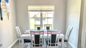 A dining area with a white table and chairs, a window with blinds, and a painting of the Leaning Tower of Pisa on the wall. - Skip the gameday/ graduation gridlock (Bryan)