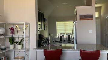 Una sala de estar moderna con un sofá gris, cojines rojos, una consola blanca con adornos y una estantería.