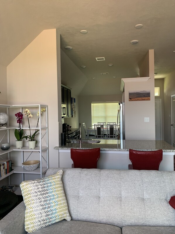 A modern living room with a gray sofa, red cushions, a white console table with decorative items, and a bookshelf.