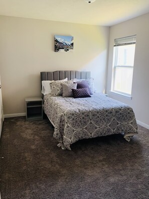 A bedroom with a bed, a nightstand, a window, and a wall-mounted picture.