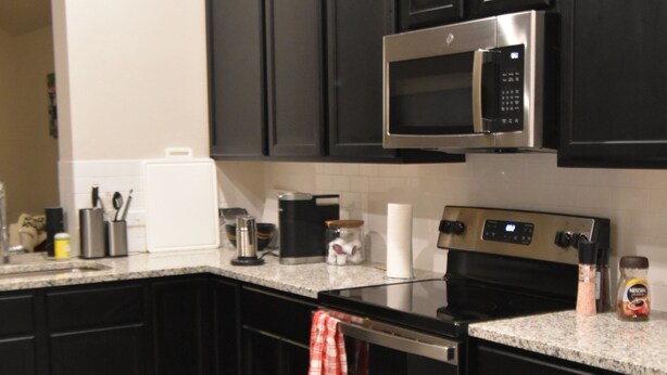 A modern kitchen with dark cabinets, stainless steel appliances, and a granite countertop. - Skip the gameday/ graduation gridlock (Bryan)