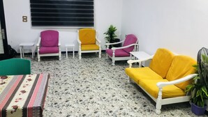 A room with a patterned tablecloth, a yellow sofa, and two armchairs with pink and yellow cushions.