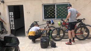 A parking area with bicycles, a car, and a building with a sign.