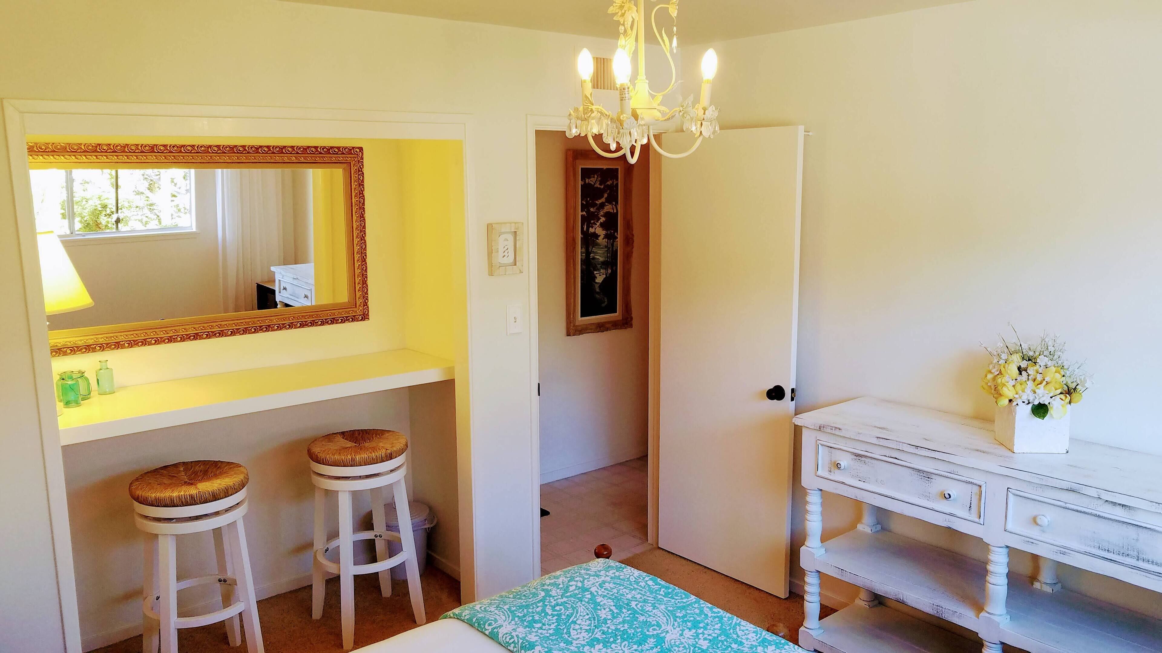 Une chambre à coucher avec un grand miroir, deux tabourets, une commode et un lustre.