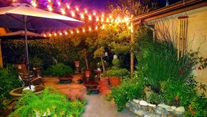Un espace extérieur aménagé en terrasse, avec des guirlandes lumineuses, une table et des chaises, des plantes en pot et un mur en pierre.