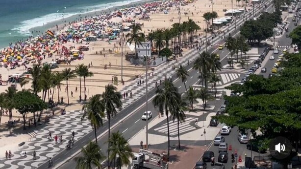A beach with a wide promenade lined with palm trees, a clear blue sky, and a cityscape in the background. - Luxury apartment by the sea (Rio de Janeiro)