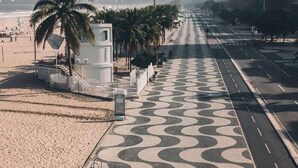A beachside promenade with a patterned walkway, palm trees, and a tall building in the background. - Luxury apartment by the sea (Rio de Janeiro)