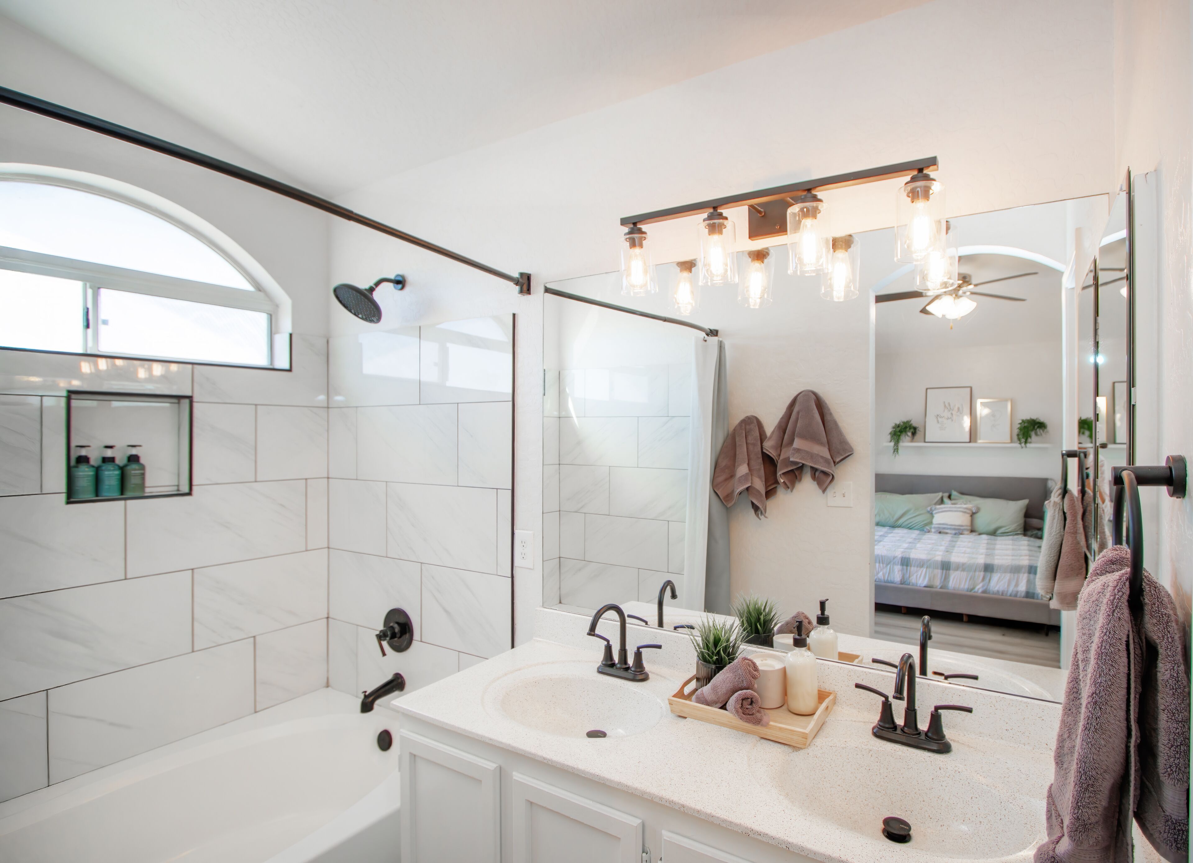 A modern bathroom with a bathtub, a shower, and a vanity with a sink and mirror. There are towels hanging on the wall and a shelf with toiletries.
