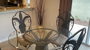 A dining area with a glass table surrounded by four chairs, a decorative vase with branches, and a chandelier.