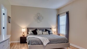 A bedroom with a bed, bedside lamps, a nightstand, a decorative wall piece, and a window with curtains.