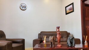 Un salon avec un canapé en cuir marron, une table basse en bois agrémentée d’objets décoratifs, une horloge murale et un tableau encadré.