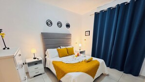 Una habitación de hotel con cama, mesitas de noche, armario y un amplio ventanal con cortinas.