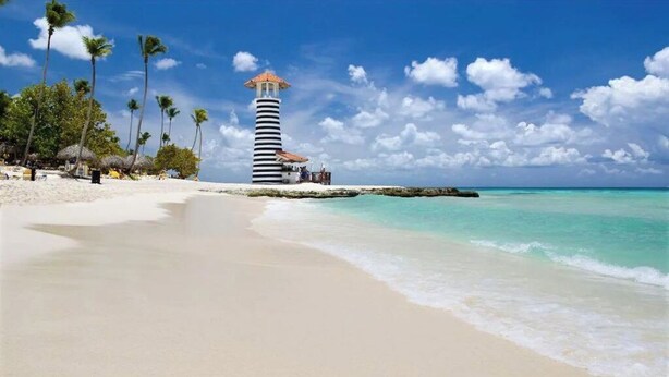 Una playa con un faro, palmeras y aguas turquesas cristalinas.