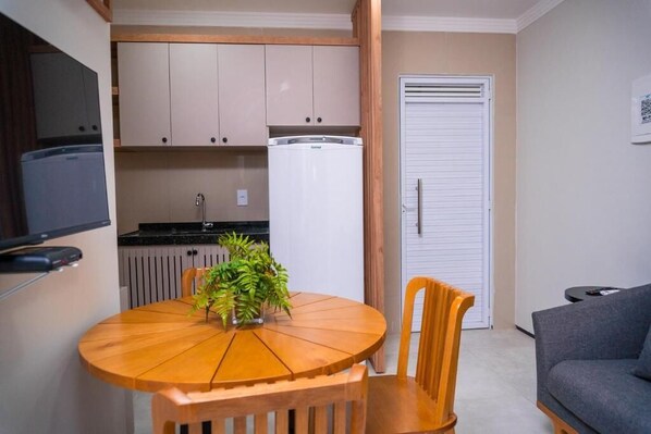 A compact kitchen with a refrigerator, a dining table with chairs, and a gray sofa. - VM Flat Residence (Camocim)