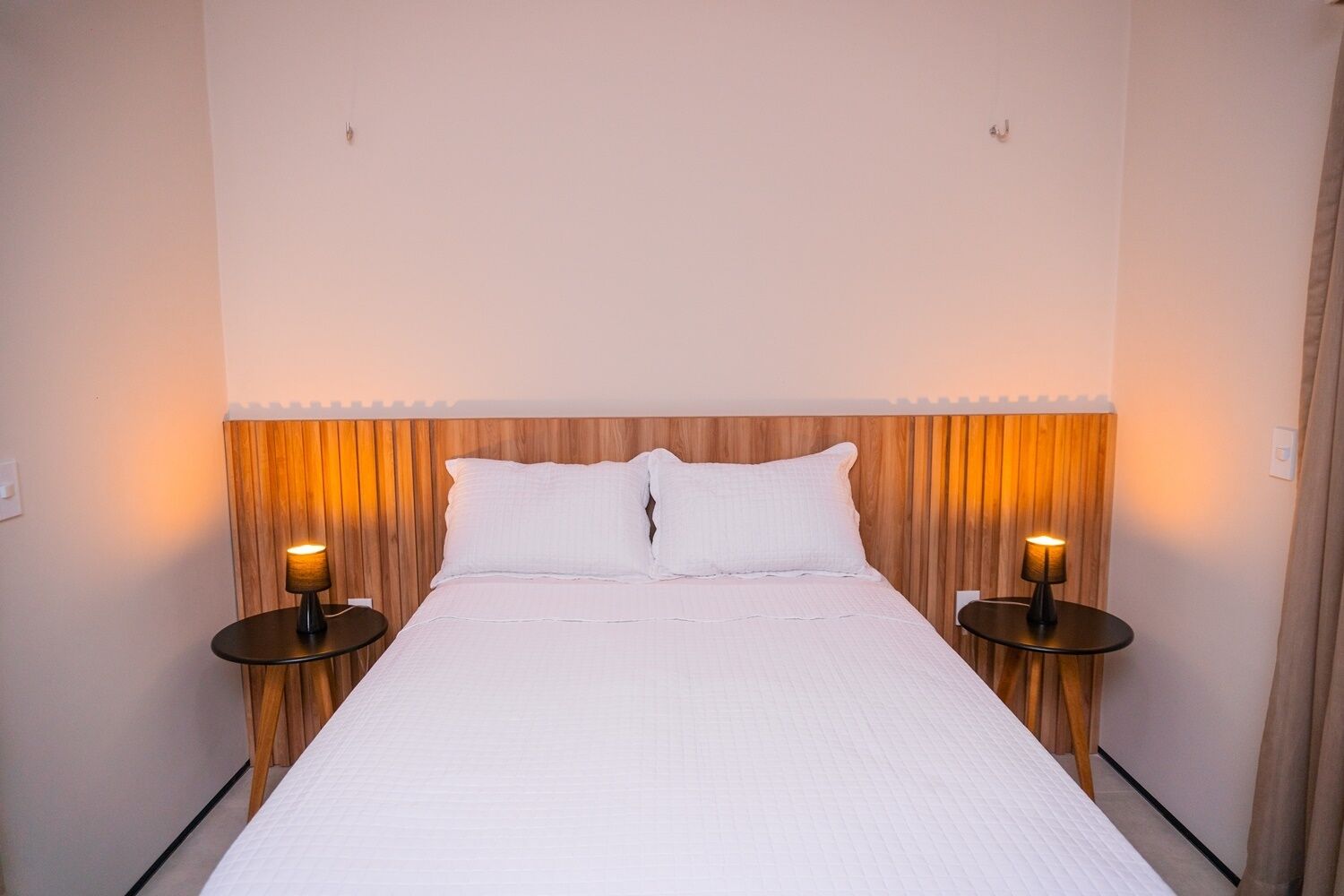 A neatly made bed with white linens, flanked by wooden headboards and two bedside lamps.