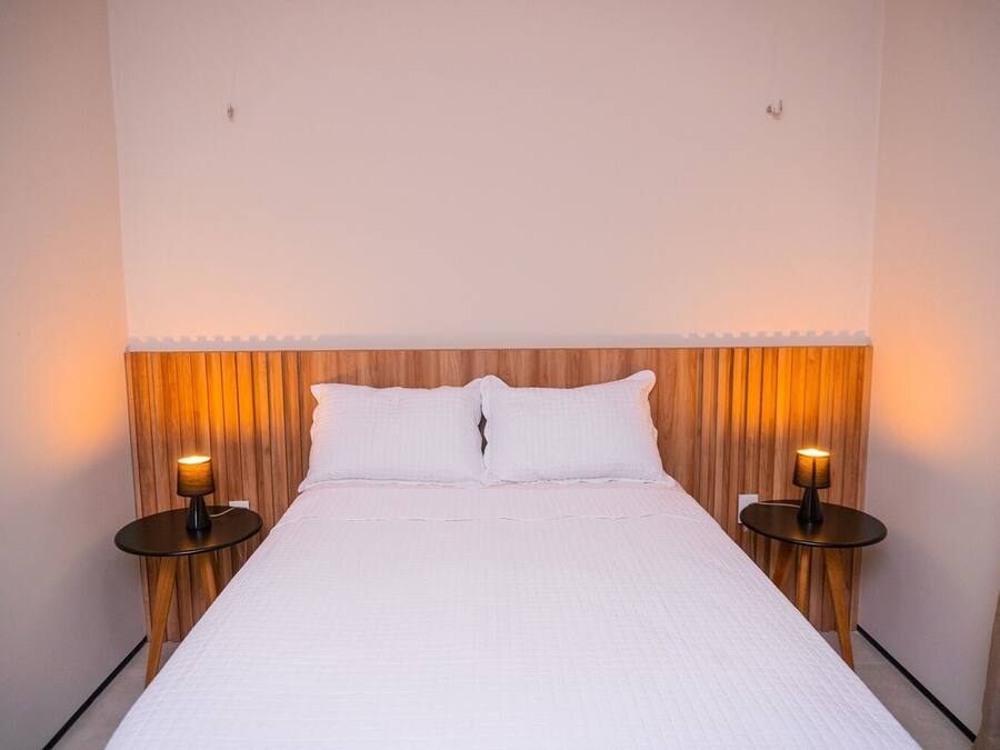 A neatly made bed with white linens, flanked by wooden headboards and two bedside lamps.